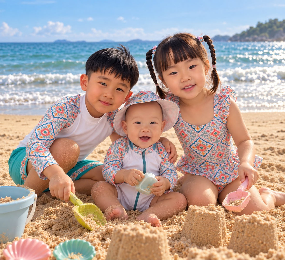 Three children in Coral Bloom swimwear building sandcastles by the sea.